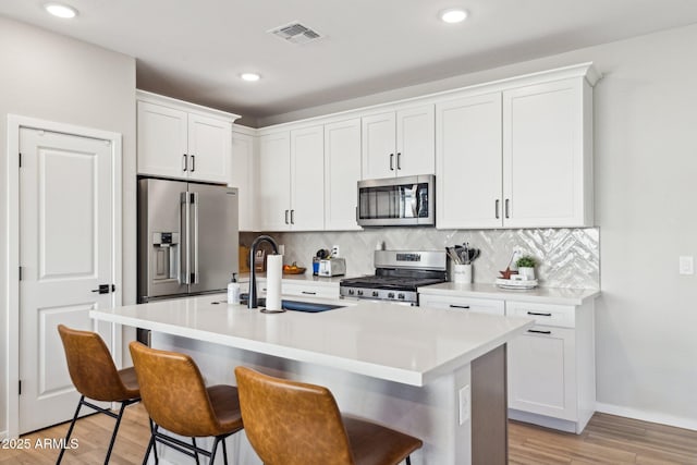 kitchen with appliances with stainless steel finishes, white cabinets, a breakfast bar, and a kitchen island with sink