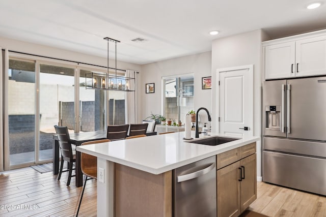 kitchen with light hardwood / wood-style floors, a center island with sink, sink, stainless steel appliances, and white cabinets