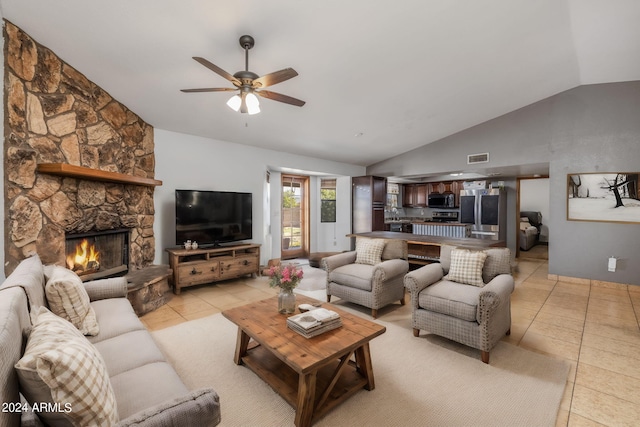 tiled living room featuring a stone fireplace, ceiling fan, and vaulted ceiling