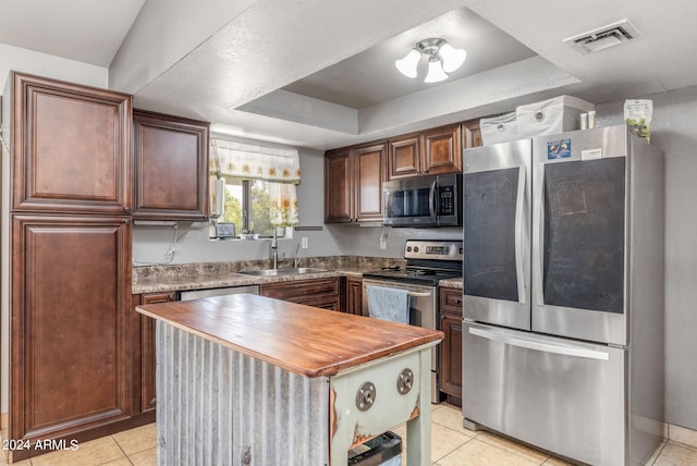 kitchen featuring butcher block counters, sink, a center island, a tray ceiling, and appliances with stainless steel finishes