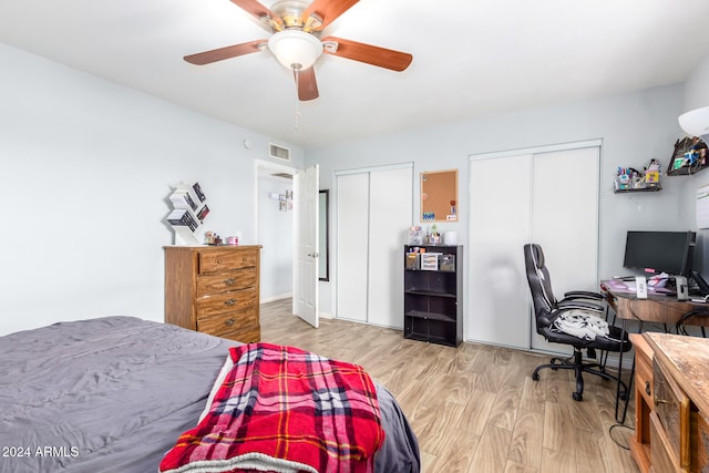 bedroom with multiple closets, light hardwood / wood-style flooring, and ceiling fan