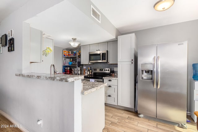 kitchen featuring light stone counters, kitchen peninsula, appliances with stainless steel finishes, light wood-type flooring, and decorative backsplash