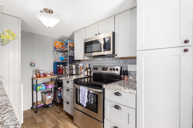 kitchen with light hardwood / wood-style flooring, tasteful backsplash, light stone countertops, white cabinetry, and appliances with stainless steel finishes