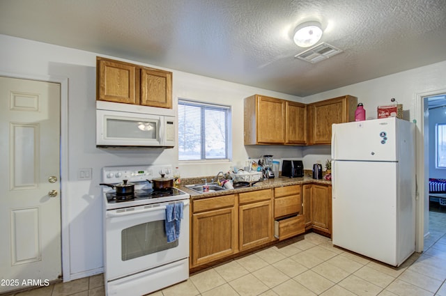 kitchen featuring white appliances, brown cabinets, visible vents, and a sink