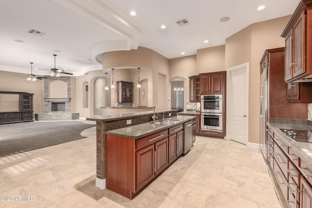 kitchen featuring arched walkways, appliances with stainless steel finishes, dark stone counters, and visible vents