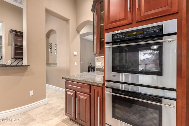 kitchen featuring baseboards, visible vents, glass insert cabinets, light stone counters, and stainless steel double oven