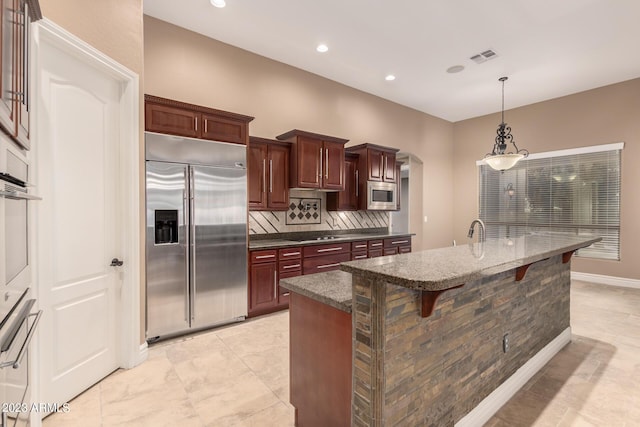 kitchen with arched walkways, decorative light fixtures, built in appliances, a kitchen bar, and backsplash