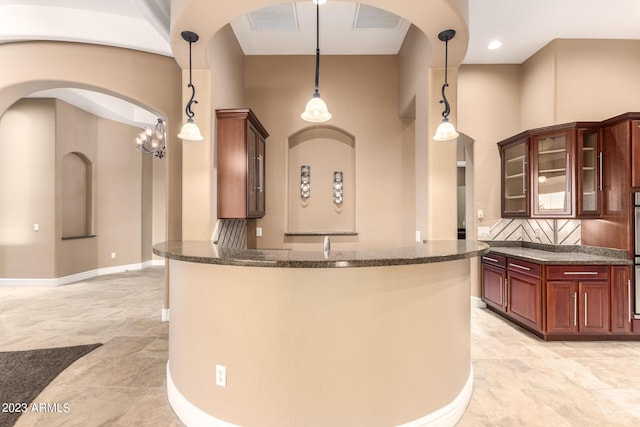 kitchen featuring baseboards, hanging light fixtures, backsplash, dark stone counters, and glass insert cabinets