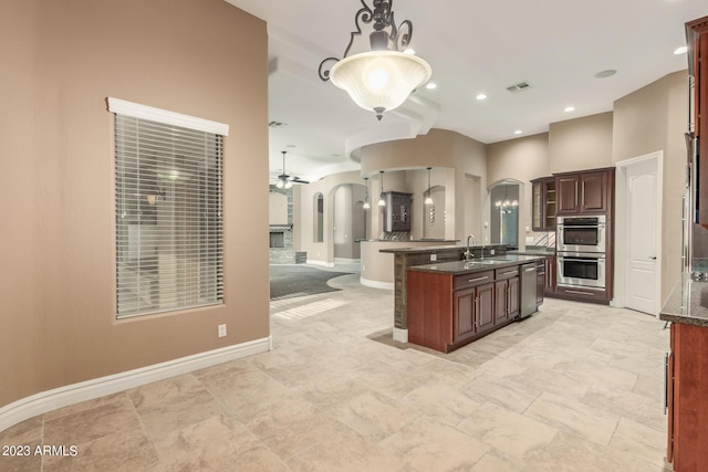 kitchen with appliances with stainless steel finishes, arched walkways, decorative light fixtures, and a kitchen island with sink