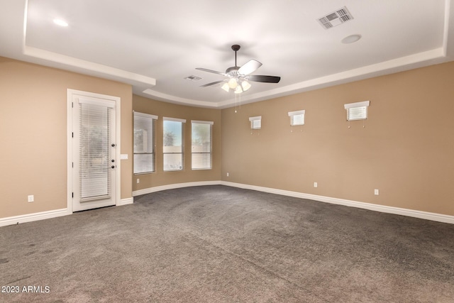 spare room featuring dark carpet, baseboards, visible vents, and a raised ceiling