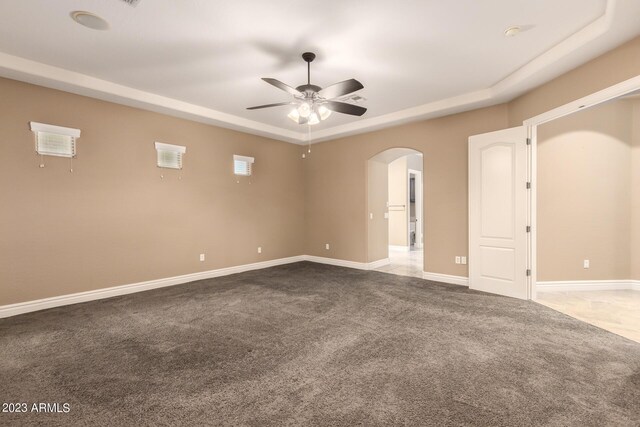 carpeted spare room featuring arched walkways, baseboards, ceiling fan, and a tray ceiling