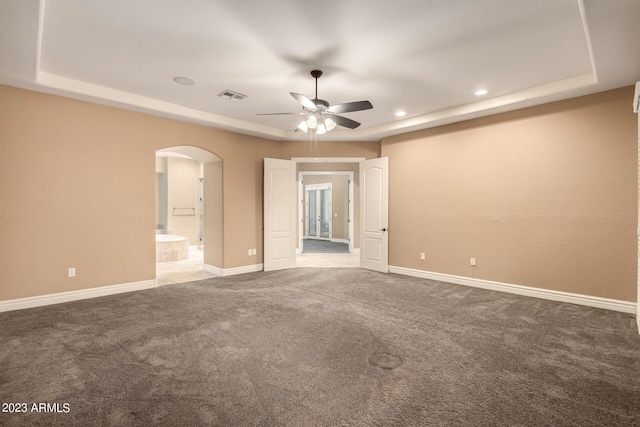 spare room featuring arched walkways, carpet floors, a raised ceiling, and visible vents