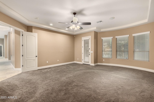 unfurnished room with a tray ceiling, carpet flooring, visible vents, and baseboards