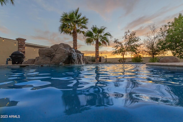 pool at dusk featuring an outdoor pool and area for grilling