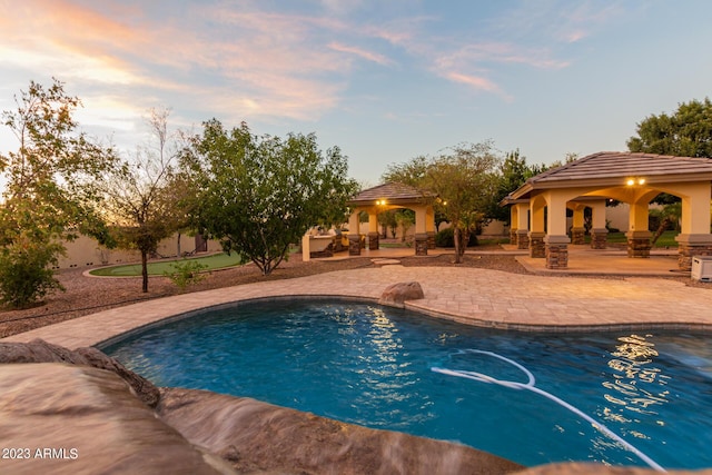 pool at dusk with an outdoor pool, a patio, and a gazebo