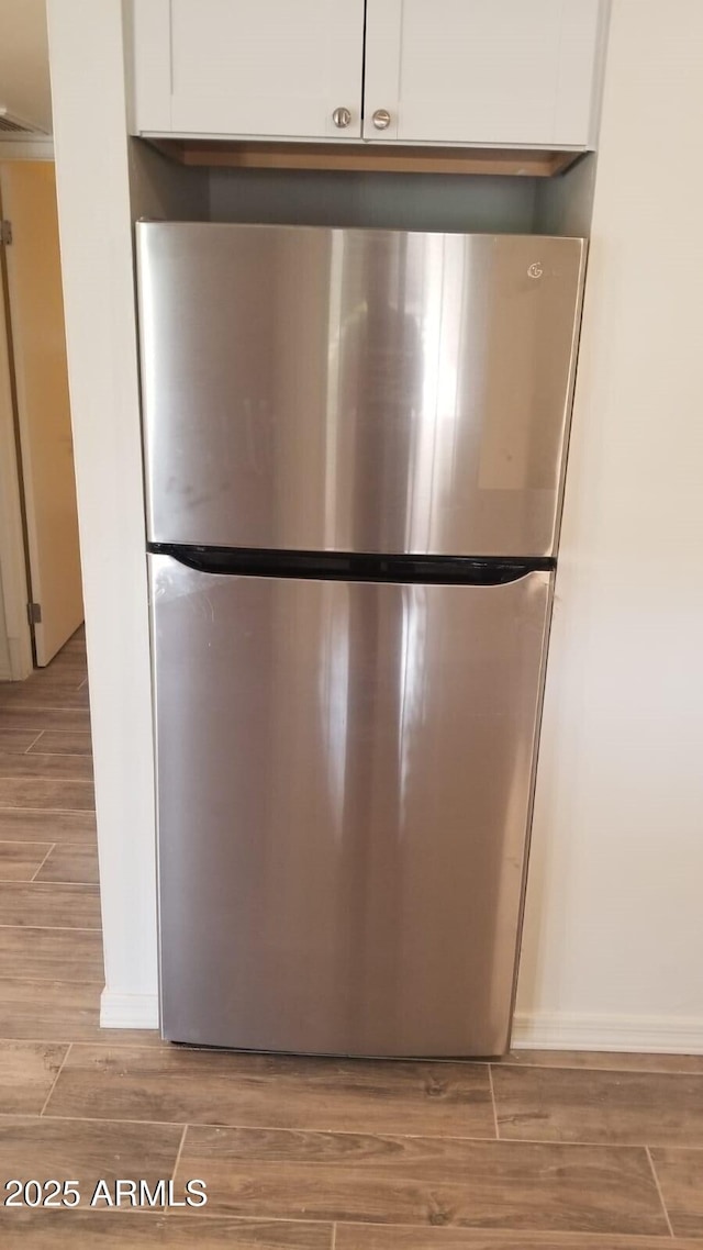 kitchen view of freestanding refrigerator, white cabinetry, light wood-style floors, and baseboards