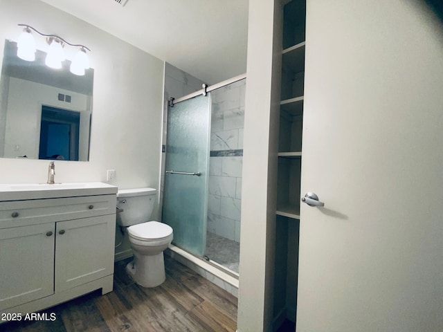 bathroom with wood finished floors, a shower stall, toilet, and vanity