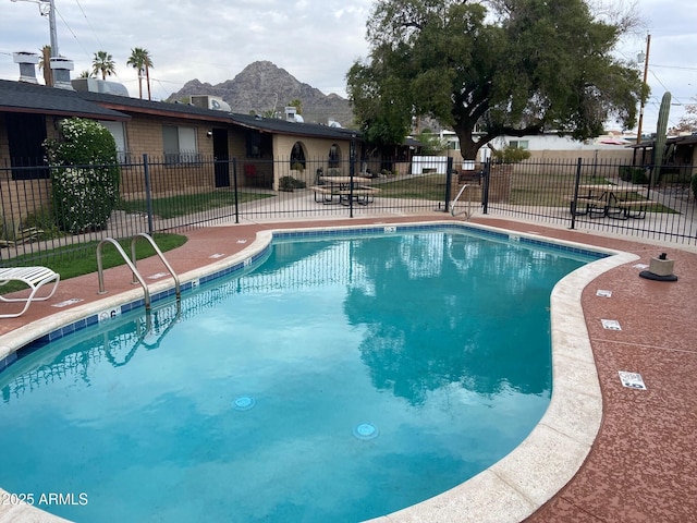 community pool with a mountain view, fence, and a patio area