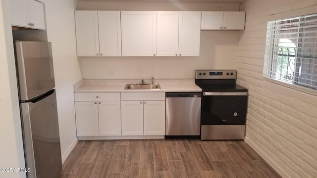 kitchen with stainless steel appliances, a sink, wood finished floors, and white cabinetry