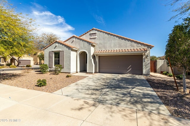 mediterranean / spanish house with driveway, a tile roof, an attached garage, fence, and stucco siding