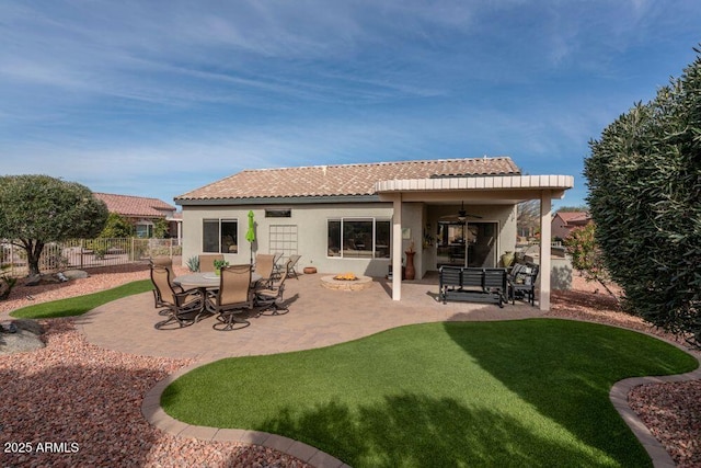 back of property featuring ceiling fan, a patio area, a fire pit, and a lawn