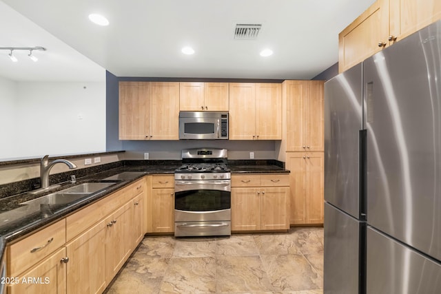 kitchen featuring light brown cabinetry, sink, dark stone counters, and appliances with stainless steel finishes