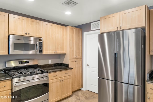 kitchen with appliances with stainless steel finishes, light brown cabinetry, and dark stone counters