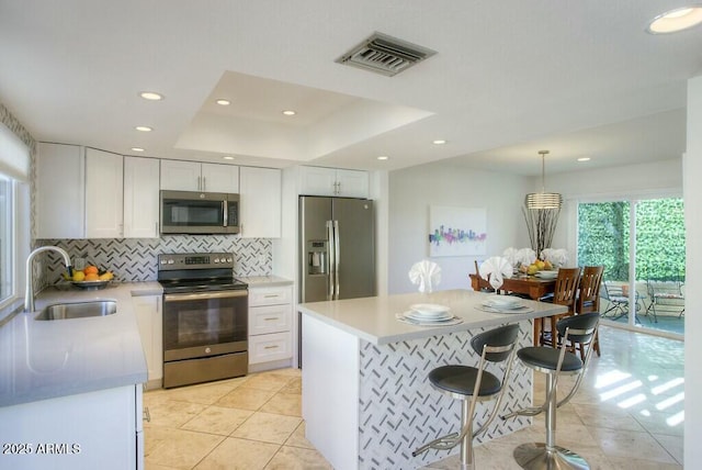 kitchen with white cabinetry, sink, hanging light fixtures, a raised ceiling, and appliances with stainless steel finishes