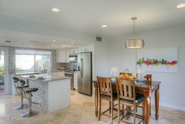 kitchen with hanging light fixtures, stainless steel appliances, light tile patterned floors, decorative backsplash, and white cabinets