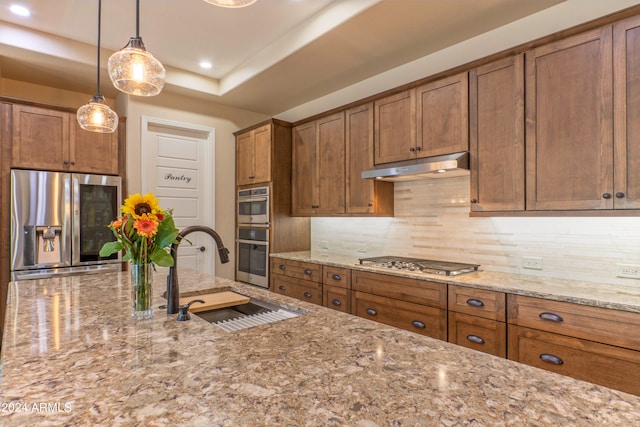 kitchen with brown cabinetry, under cabinet range hood, stainless steel appliances, and a sink