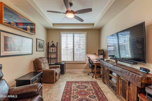 home office with a tray ceiling, a ceiling fan, and baseboards