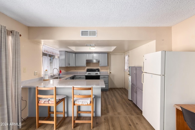 kitchen featuring a breakfast bar, dark hardwood / wood-style floors, sink, kitchen peninsula, and white appliances