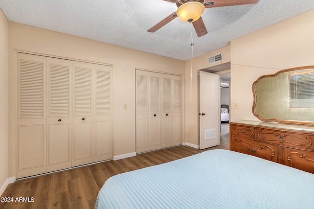 bedroom with ceiling fan, multiple closets, a textured ceiling, and dark hardwood / wood-style flooring