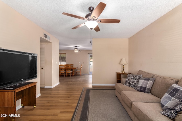 living room with ceiling fan, a textured ceiling, and dark hardwood / wood-style flooring