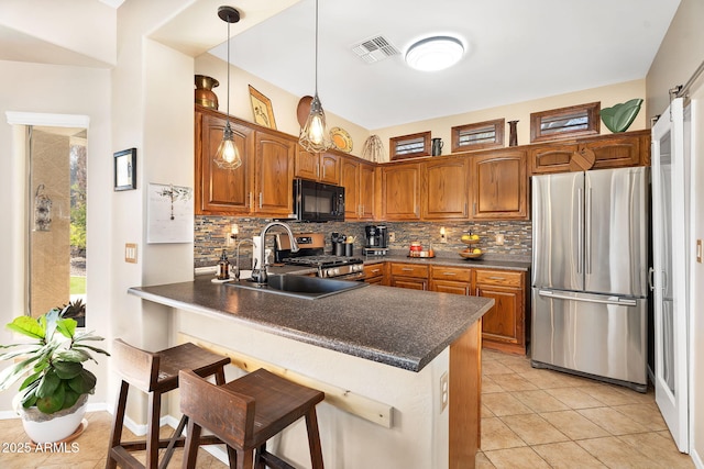 kitchen featuring a peninsula, appliances with stainless steel finishes, dark countertops, brown cabinets, and backsplash