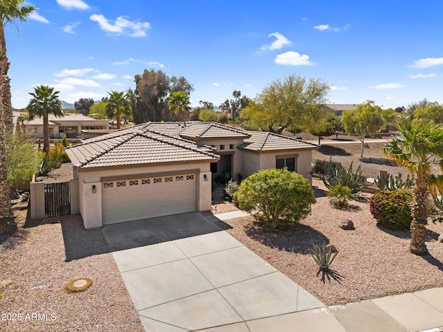 view of front of house with a tile roof, concrete driveway, stucco siding, an attached garage, and a gate