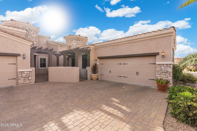 mediterranean / spanish-style home with a garage, stone siding, a gate, decorative driveway, and stucco siding