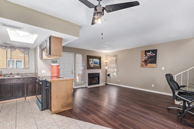 interior space with sink, a tiled fireplace, light hardwood / wood-style flooring, a skylight, and ceiling fan