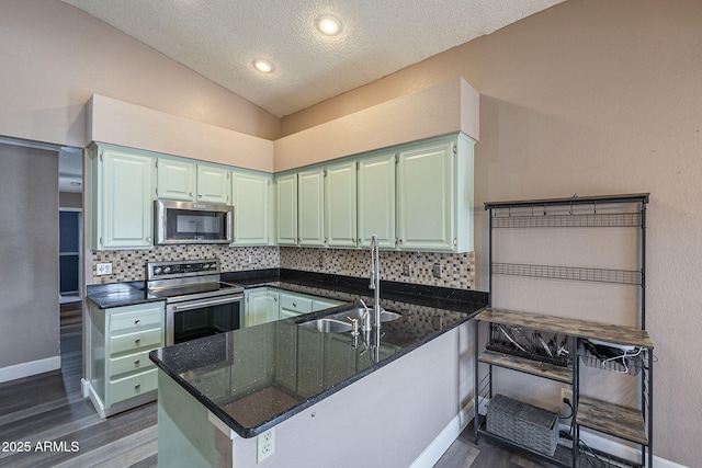 kitchen with stainless steel appliances, a peninsula, a sink, vaulted ceiling, and decorative backsplash