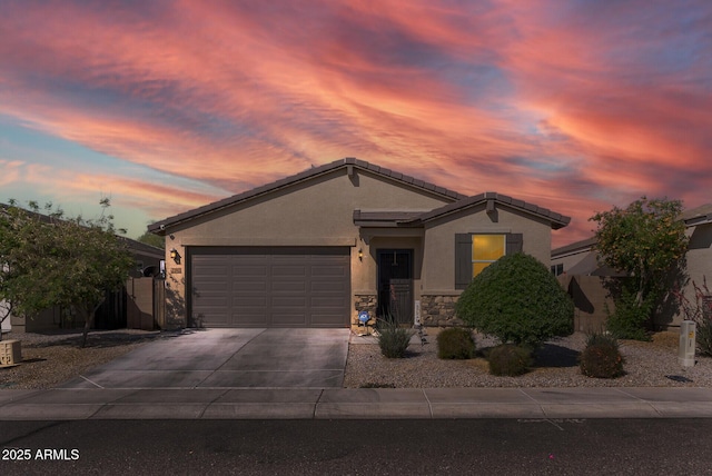 view of front of property featuring a tile roof, a garage, driveway, stone siding, and stucco siding