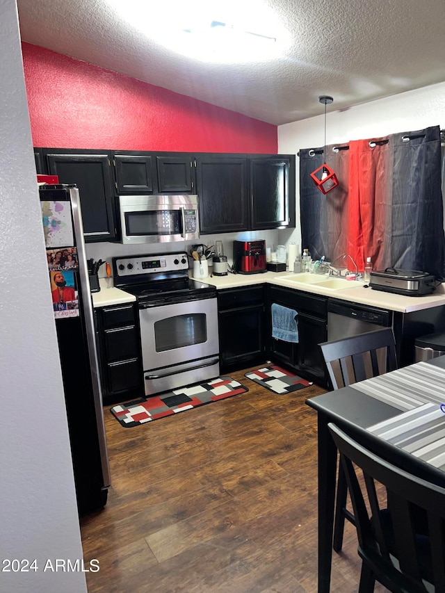 kitchen featuring dark hardwood / wood-style flooring, appliances with stainless steel finishes, vaulted ceiling, sink, and a textured ceiling