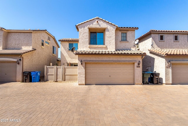 mediterranean / spanish home featuring fence, a tile roof, stucco siding, decorative driveway, and a garage