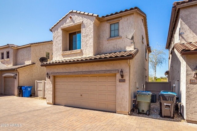 view of front of home with fence, a tiled roof, stucco siding, decorative driveway, and an attached garage