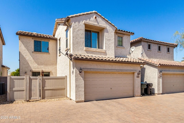 mediterranean / spanish house featuring stucco siding, a tile roof, decorative driveway, fence, and a garage