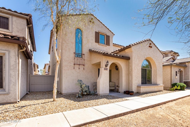 mediterranean / spanish-style home with a tile roof, fence, and stucco siding
