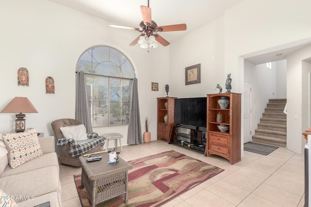living room featuring stairs, light tile patterned floors, a ceiling fan, and a towering ceiling