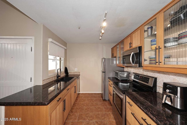 kitchen with tasteful backsplash, dark stone countertops, appliances with stainless steel finishes, a peninsula, and a sink