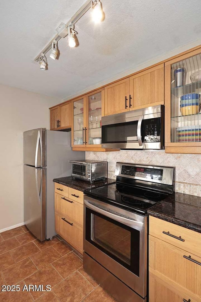 kitchen featuring stainless steel appliances, tasteful backsplash, and dark stone countertops