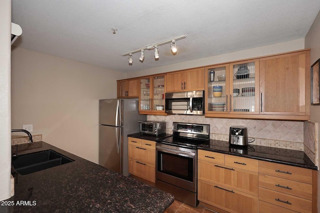 kitchen with sink, stainless steel appliances, dark stone countertops, decorative backsplash, and light tile patterned flooring