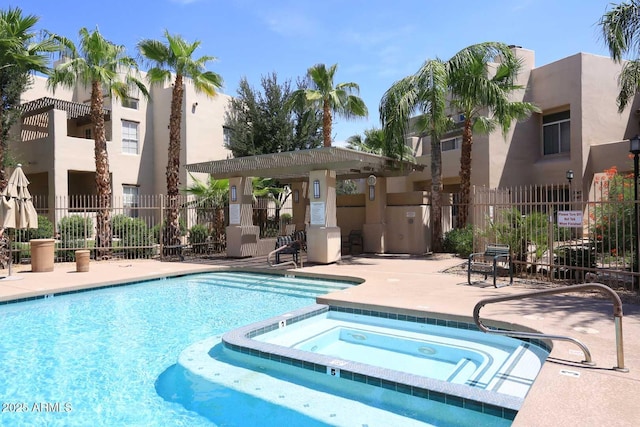 community pool with a patio area, a hot tub, and fence